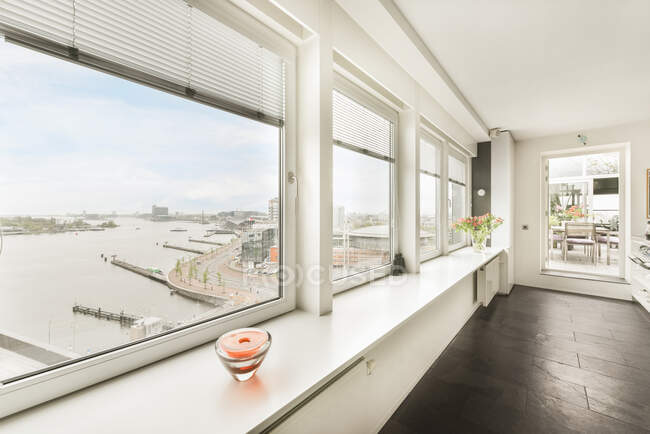 Interno di appartamento moderno con pareti bianche e grandi finestre panoramiche che si affacciano sul paesaggio urbano con canale — Foto stock