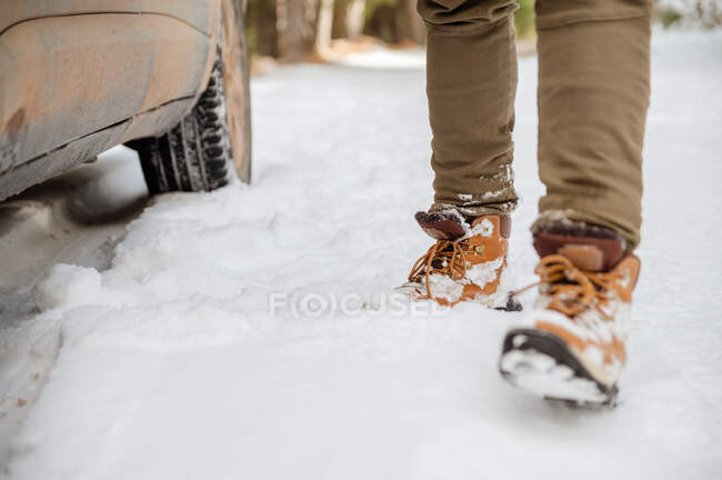 Анонимный мужчина в теплой одежде выходит из машины, припаркованной на снежной дороге в зимних лесах — стоковое фото