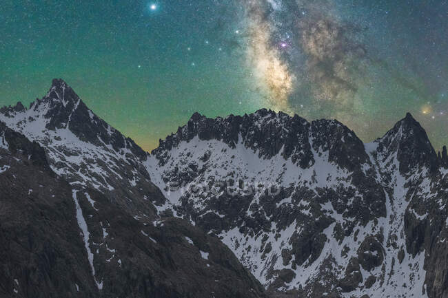 Небесна галактика з міжзоряним газом над грубою величною горою з снігом увечері. — стокове фото