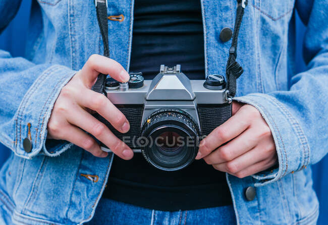 Обрізати невпізнавану жінку-фотографа в джинсовій куртці і джинсах, що стоять з старовинною фотокамерою — стокове фото