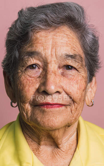 Donna anziana con capelli corti grigi e occhi marroni che guarda la fotocamera su sfondo rosa in studio — Foto stock