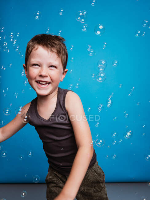 Preteen ragazzo guardando lontano in studio con volare sapone bolle su sfondo blu — Foto stock