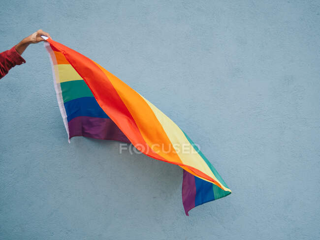 Anonymer homosexueller Mann steht mit LGBT-Regenbogenfahne in der Nähe der blauen Mauer in der Stadtstraße — Stockfoto