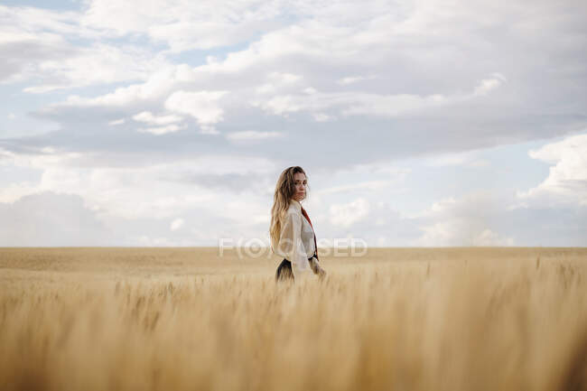 Side view of young mindful female in formal wear with tie looking at camera among spikes in countryside — Stock Photo