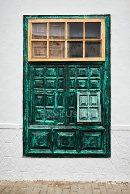 Unconventional window with ornamental green shutters located on white building wall on town street — Stock Photo