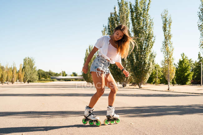 Vista lateral de la hembra en forma de patines que muestra truco en la carretera en la ciudad en verano - foto de stock