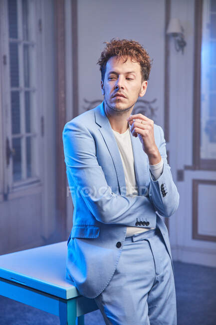 Задумчивый стильный мужчина в костюме сидит за столом в шикарной комнате и смотрит в сторону — стоковое фото