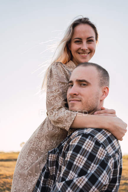 Cooler Freund umarmt lächelnde Freundin, während er in die Kamera schaut — Stockfoto