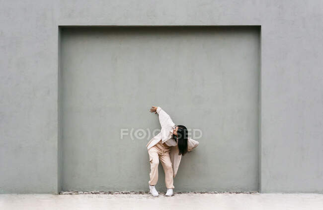 Energetic female dancer moving and performing in city street while leaning on gray wall — Stock Photo
