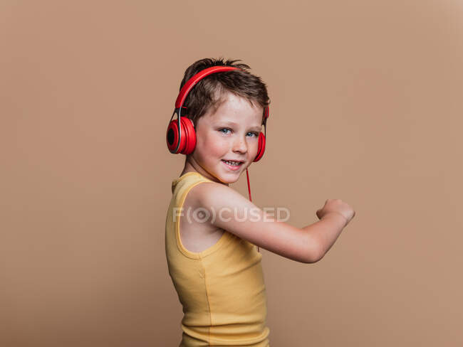 Satisfied preteen boy in red headphones listening to music on brown background in studio — Stock Photo