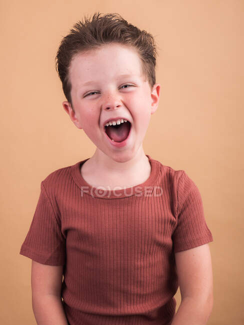 Задоволена дитина в повсякденному одязі з коричневим волоссям дивиться на камеру з зубною посмішкою і нахиленою головою — стокове фото