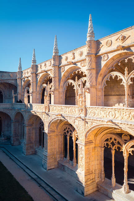 Дугообразные стены с резными орнаментами образуют внутренний двор Иеронимосского монастыря против безоблачного голубого неба в солнечный день в Лиссабоне, Португалия — стоковое фото