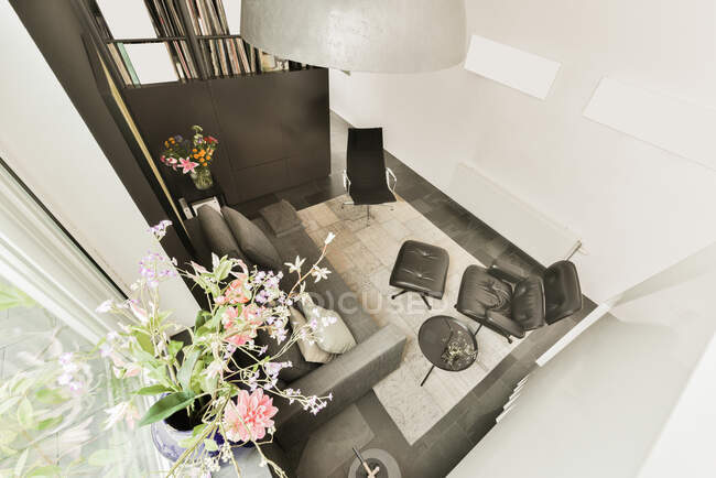 Зверху зручне шкіряне крісло з пішохідним відпочинком розміщене біля дивана в невеликій лаунж-зоні, прикрашеному квітами в сучасній квартирі в стилі лофт — стокове фото