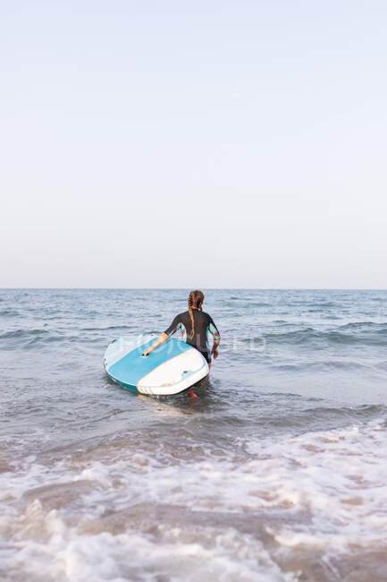 Back view of unrecognizable female in swimsuit standing with SUP board in sea water in summer — Stock Photo
