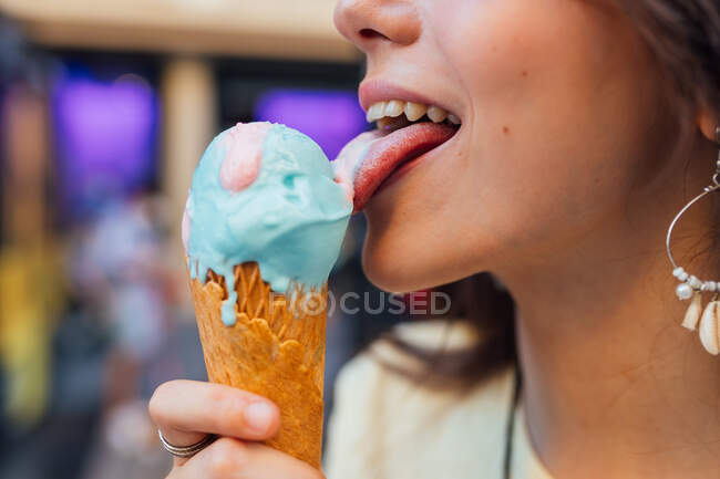 Cortar jovem fêmea lambendo saboroso gelato em waffle cone na cidade no fundo borrado — Fotografia de Stock