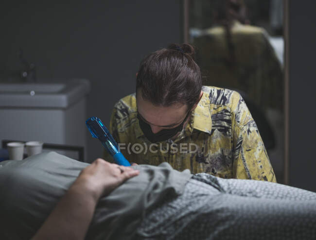 Focused male tattoo master using professional machine and making tattoo on hand of unrecognizable client in salon — Stock Photo