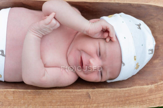 Вид сверху на симпатичного маленького младенца, спящего в деревянном тубе, установленном на зеленой траве — стоковое фото