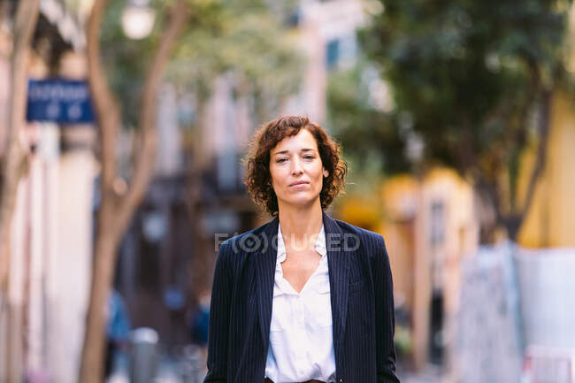 Позитивна жінка в стильному одязі, що йде по вулиці посміхаючись дивиться на камеру — стокове фото