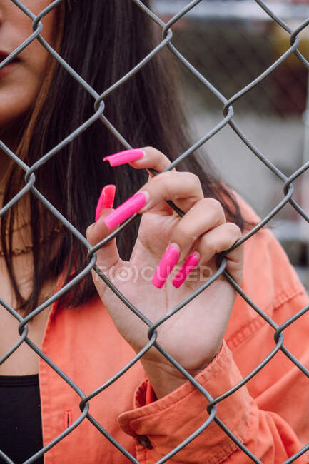 Crop view of hand of stylish female with bright long manicure standing near metal fence — Stock Photo