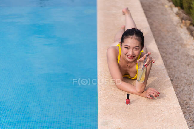 Сверху азиатка в жёлтом бикини, лежащая возле бассейна и загорающая, наслаждаясь летним отдыхом на курорте — стоковое фото