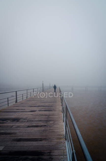 Personne méconnaissable se promenant sur un quai en bois dans un épais brouillard le matin à Lisbonne, Portugal — Photo de stock
