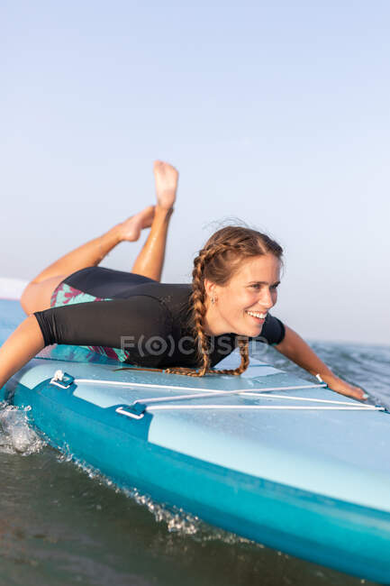 Surfista feminina encantada deitada na placa SUP e flutuando na água calma do mar no dia ensolarado — Fotografia de Stock