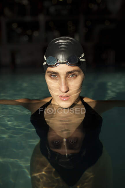 Молода красива жінка в критому басейні, одягнена в чорний купальник, дивиться на камеру — стокове фото