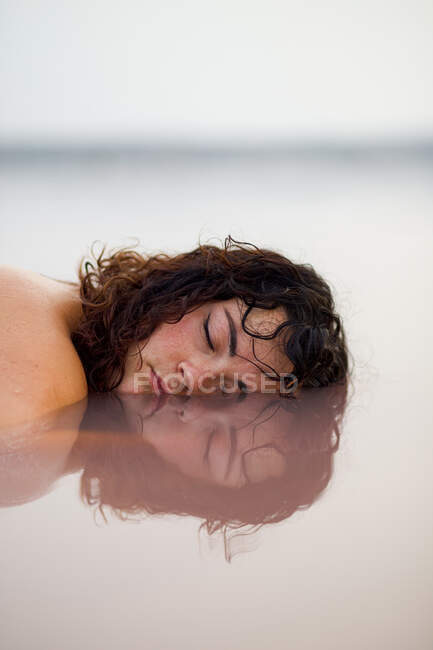 Donna tranquilla con occhi chiusi che si trova con metà della faccia in acqua di stagno rosa in estate — Foto stock