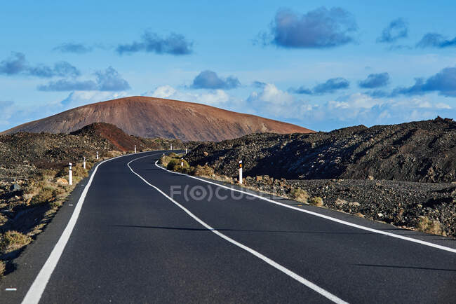Geradlinige Asphaltstraße durch Feld in Richtung Bergfahrt am Morgen auf Fuerteventura, Spanien — Stockfoto
