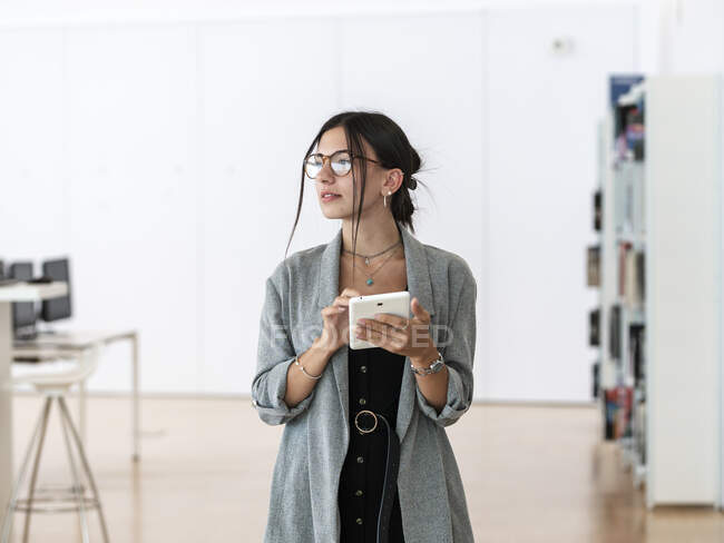 Жінка в окулярах, використовуючи планшет, стоячи в просторому робочому місці і працюючи над проектом — стокове фото