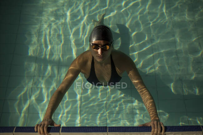 Junge schöne Frau am Bordstein des Hallenbades, in schwarzem Badeanzug, im Wasser treibend — Stockfoto
