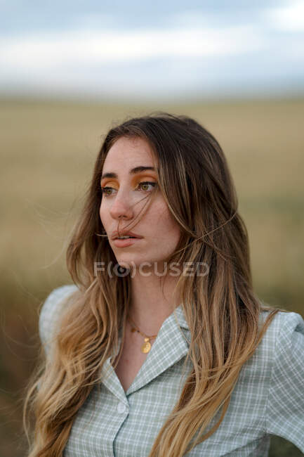 Young mindful female looking away on road near meadow under cloudy sky in evening in countryside — Stock Photo