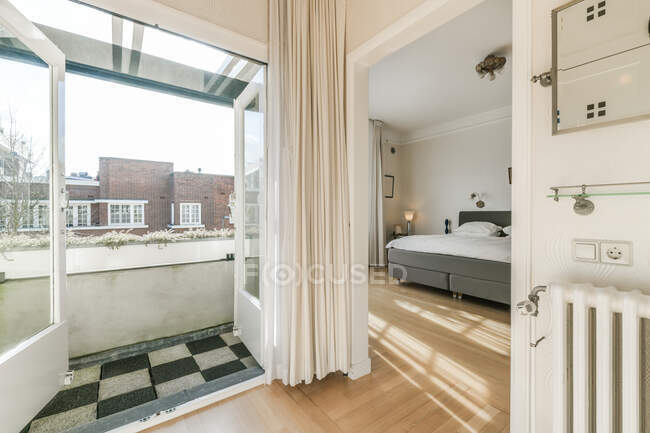 Interior de piso contemporáneo en estilo minimalista con amplio dormitorio y balcón con puertas abiertas - foto de stock