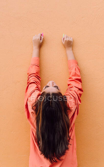 Back view of young woman in modern outfit with bright long manicure raising hands against orange background — Stock Photo