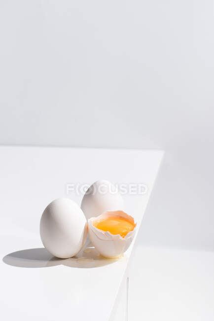 Високий кут цілого і розбитого яйця з жовтком в оболонці, розміщені на краю столу на білому тлі в студії — стокове фото