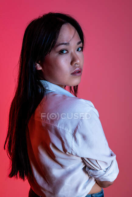 Side view of confident ethnic female model in trendy clothes looking at camera in studio on pink background — Stock Photo