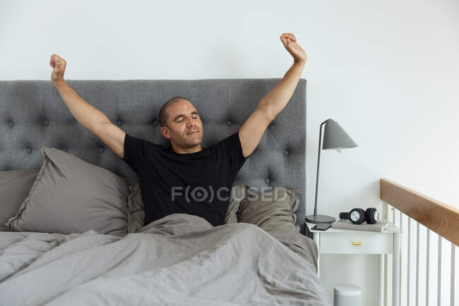 Carefree male stretching arms on bed while enjoying morning with closed eyes at home — Stock Photo