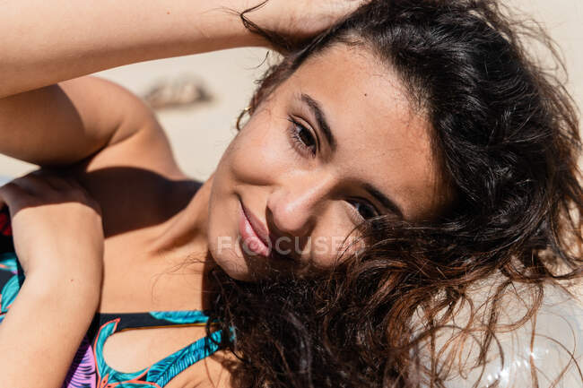 Portrait of happy female in swimsuit lying on inflatable mattress on sandy seashore and sunbathing on sunny day during summer vacation — Stock Photo