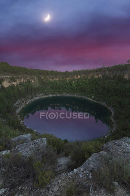 Pintoresca vista de la laguna reflejando árboles creciendo en montes bajo la luna en Cuenca España - foto de stock
