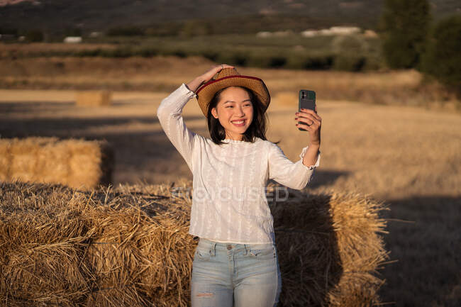 Жінка фотографується на мобільному телефоні, стоячи в сухому полі влітку під час заходу сонця — стокове фото
