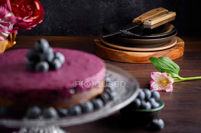 Смачний чорничний торт з пурпуровим кремом, прикрашеним свіжими ягодами, подається на скляному столику з квітами. — стокове фото