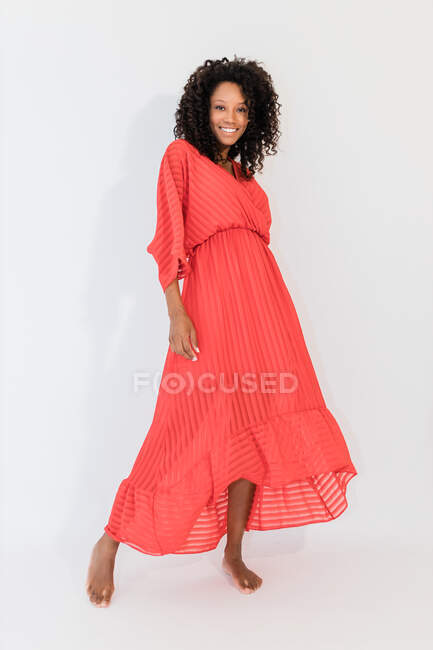 Smiling barefoot ethnic woman with curly hair in trendy dress with striped ornament looking at camera — Stock Photo