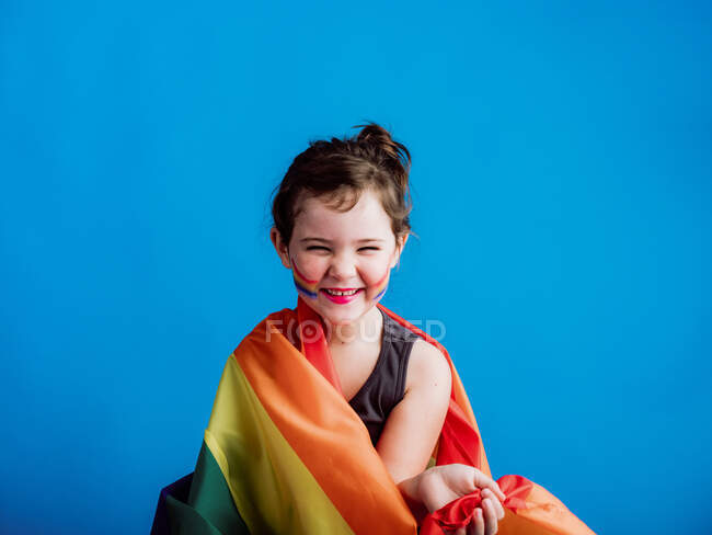 Smiling girl with painted cheek with multicolored flag on vivid blue background — Stock Photo