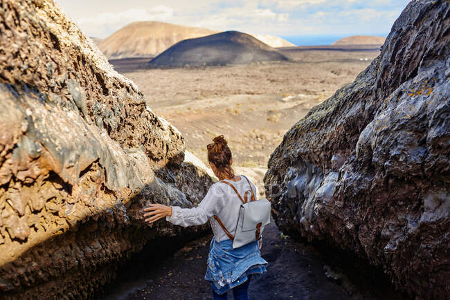 Vue arrière de la femme en vêtements décontractés touchant la formation de pierre tout en marchant dans les hauts plateaux pendant le voyage à Fuerteventura, Espagne — Photo de stock