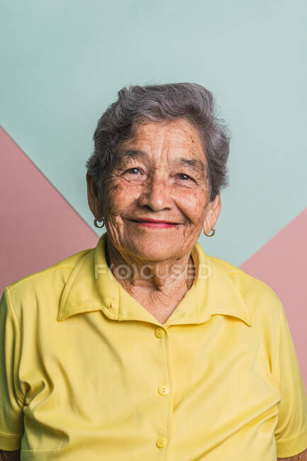 Elderly female with short gray hair and brown eyes looking at camera on pink and blue background in studio — Stock Photo