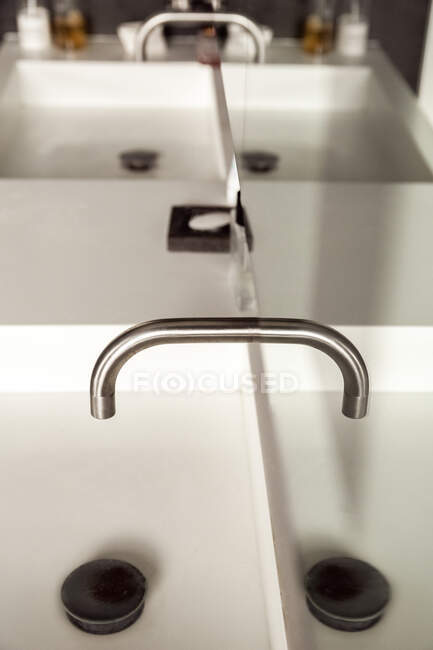 Сверху металлический кран поверх белой керамической раковины, отражающейся в зеркале в ванной комнате, выполненной в минимальном стиле — стоковое фото
