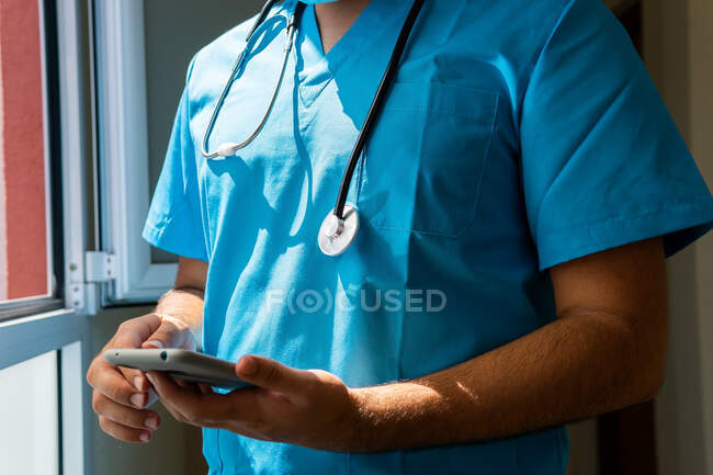 Unrecognizable crop doctor in uniform using mobile phone while standing in corridor near window in hospital — Stock Photo
