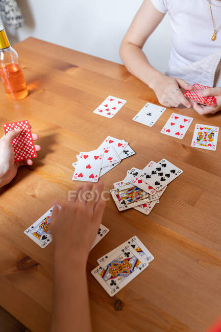 Desde arriba anónimo encantado pareja LGBT de mujeres sentadas en la mesa y jugando a las cartas mientras entretienen en el fin de semana en casa - foto de stock