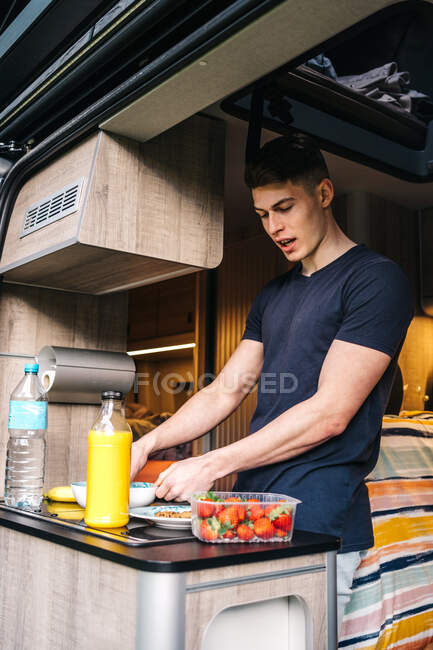 Junge männliche Reisende bereiten in den Sommerferien ein gesundes Frühstück mit natürlichem Saft und frischen Beeren im Wohnmobil zu — Stockfoto