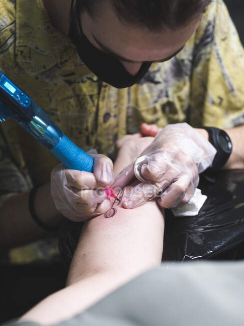 Master del tatuaggio maschile focalizzato utilizzando una macchina professionale e rendendo il tatuaggio a portata di mano del cliente irriconoscibile nel salone — Foto stock